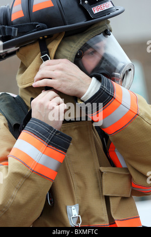 A fire fighter putting on and latching his helmet in full gear Stock Photo