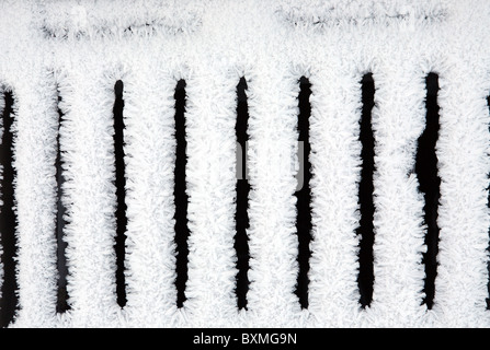 Snow crystals form a pattern on the grid of a roadside drain cover. England, UK Stock Photo