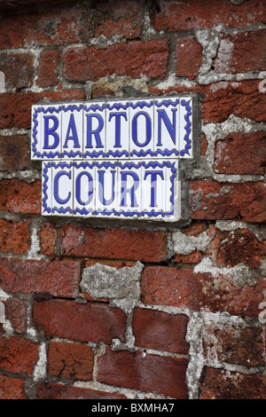 A sign composed of individual glazed ceramic tiles attached to a red brick wall.  The mortar has been repaired poorly. Stock Photo