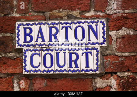 A sign composed of individual glazed ceramic tiles attached to a red brick wall.  The mortar has been repaired poorly. Stock Photo
