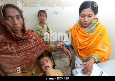 Pakistan after the flood. Doctor Sahira Bano examines a patient watched by her family, she takes the pulse Stock Photo