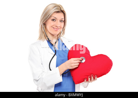 A smiling female doctor examining a red heart shaped pillow with a stethoscope