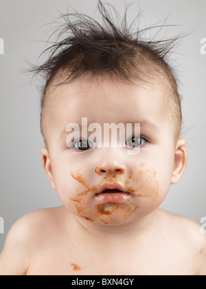 Artistic portrait of a seven month old baby boy with messy hair and smudged with food face
