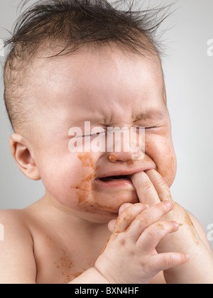 Artistic portrait of a crying seven month old baby boy with messy hair and smudged with food face
