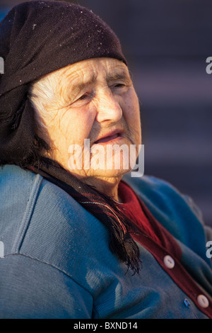 Portrait of an elderly Romanian woman wearing a scarf sitting outside, looking away with a sad expression. Stock Photo