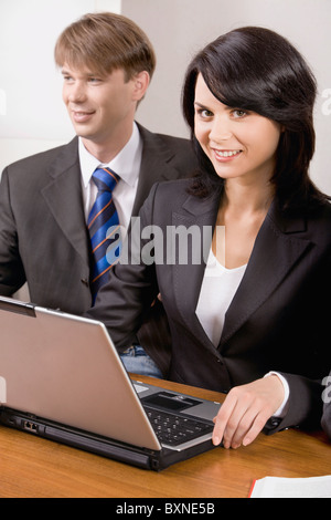 Responsible woman is smiling and sitting at the table with business man near by Stock Photo