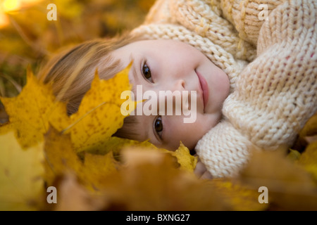 Head of girlie lying on golden leaves in autumn with peaceful expression