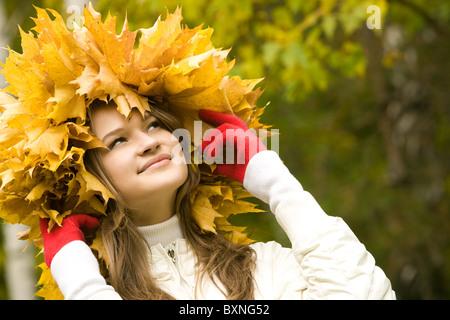 Portrait of smiling young woman touching wreath of maple leaves Stock Photo