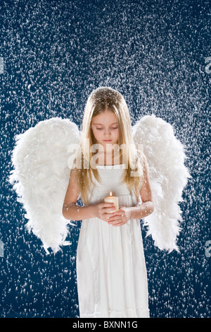 Portrait of calm girl wearing angel wings and holding candle in flurry snowfall Stock Photo