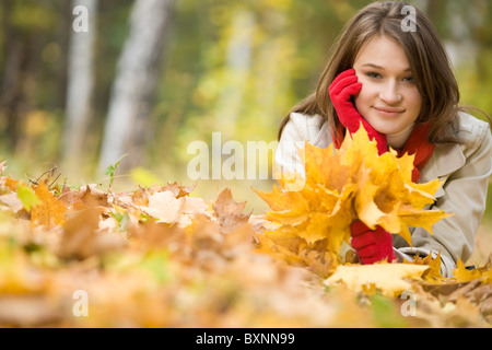 Image of pretty girl lying on ground covered with yellow dry leaves in fall