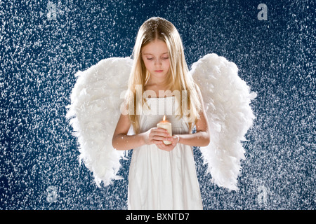 Photo of sad angel holding burning candle while standing under snowfall Stock Photo