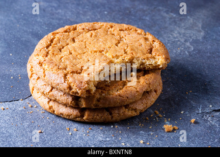 Three ginger biscuits stacked with the top one having a bite taken out of it and placed on a piece of slate Stock Photo