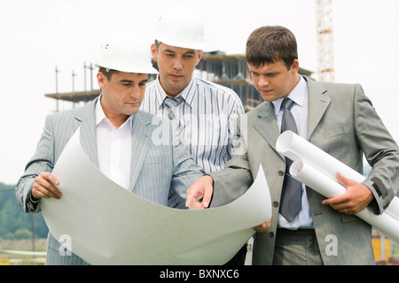 Image of three businessmen looking at architectural project at meeting Stock Photo