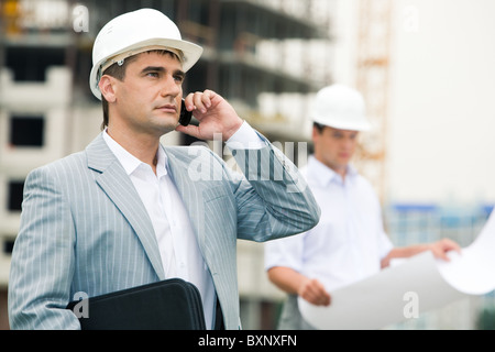 Photo of confident foreman speaking on the cellular phone on the background of employee Stock Photo