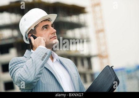 Image of serious engineer calling on his mobile and looking upwards at building site Stock Photo