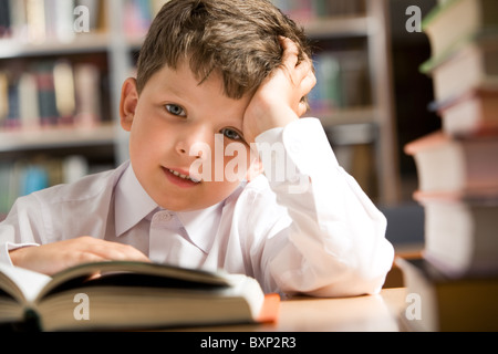 Photo of young boy sitting at the table in the library Stock Photo