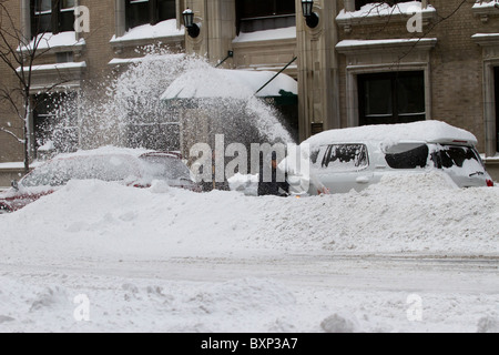 A man using a snow blower to dig out his car in the aftermath of a late December blizzard that dumped two feet of snow on NYC. Stock Photo