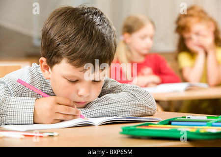 Portrait of bored pupil putting his head on desk and drawing something in copybook at lesson Stock Photo