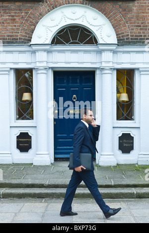 Businessman using mobile cellphone passes Georgian architecture doorway in Merrion Square, Dublin city centre, Ireland Stock Photo