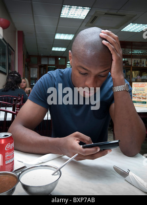 Man using the Internet in his smart mobile phone in a fast food restaurant Stock Photo