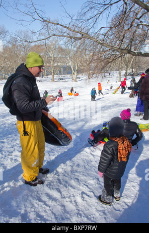 A boy waits for this father to finish texting so he can go sledding in Riverside Park on the day after a blizzard hit New York Stock Photo