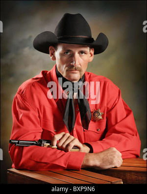 handsome Western cowboy with gun and badge sitting in studio Stock Photo