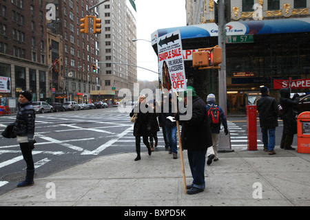 An old man holding a billboard for Fur & Shearling coats sale at the corner of Sixth ave & 57th st in blizzard in Manhattan, NYC Stock Photo