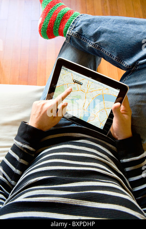 Man relaxing at home using an Apple iPad to look at Google maps on his lap. Stock Photo