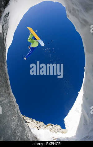 View from below of snowboarder jumping over rocky mountainside in winter Stock Photo