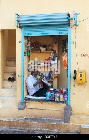 Indian man sitting reading inside a rural South Indian village shop. Andhra Pradesh, India Stock Photo