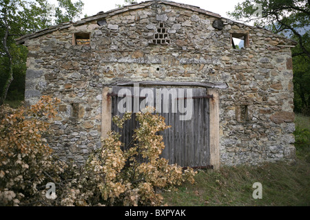 The front of a derelict stone building with felled oak branches in South-East France. Stock Photo