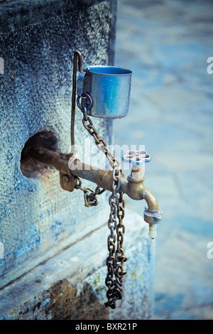 Vertical view of a old water tap with a metal cup. Stock Photo