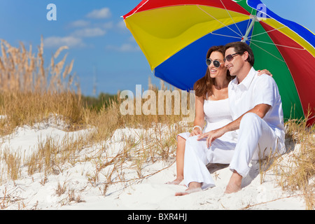 Man and woman romantic couple under a colorful sun umbrella or parasol on a beach Stock Photo