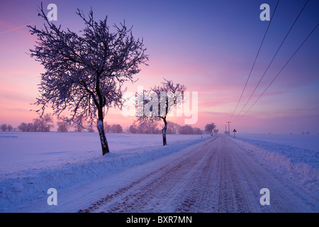 snow covered cobblestone country road in a winter landscape at dusk near Halle (Saale); Germany Stock Photo
