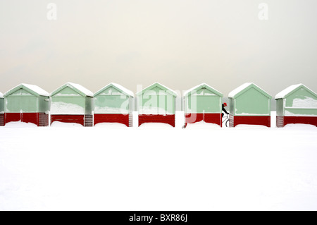 A cyclist passes a row of beach huts covered in snow Stock Photo
