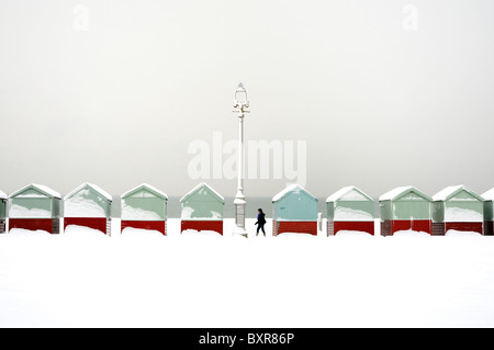 A walker passes a row of beach huts covered in snow Stock Photo