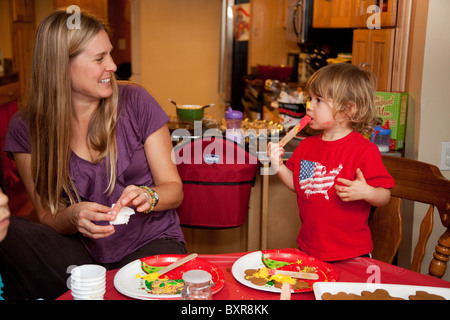 A White mother supervises her messy White/Mexican 2-year-old son decorating Christmas cookies Stock Photo