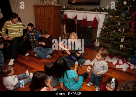Mothers and children gather around a woman playing guitar and singing Christmas carols at a Christmas party at home Stock Photo