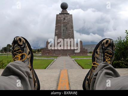A traveller with one feet each across the Equator line marked on the ground in the park 'Mitad del Mundo' near Quito, Ecuador. Stock Photo