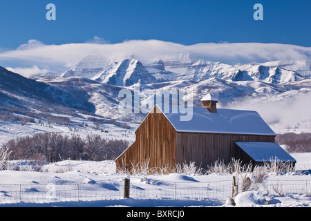 Old barn in foreground, of a beautiful winter landscape, with large mountain in the background surrounded by fog and clouds. Stock Photo