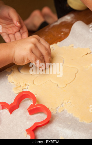 Child's hands cutting out sugar cookie dough at the kitchen table Stock Photo