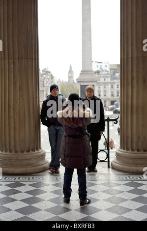 A lady photographing her two friends in the entranceway to the National Gallery with Big Ben in the distance, London, England