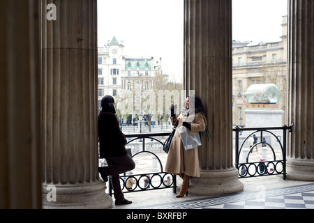 A lady photographing her boyfriend in the entranceway to the National Gallery, Trafalgar Square, London, England, UK