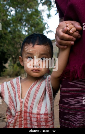 A young Burmese boy whose family fled war atrocities in Burma is holding his mother's hand in Ban Tha Ta Fang, Thailand.. Stock Photo