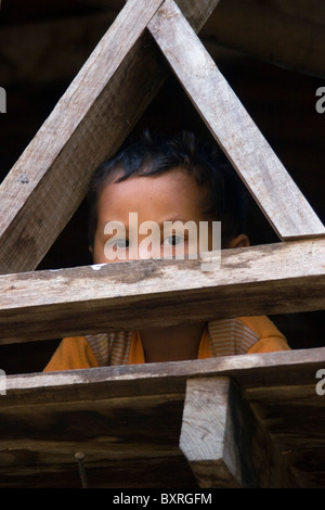 A young Burmese boy whose family fled war atrocities in Myanmar is looking out from his home in Ban Tha Ta Fang, Thailand. Stock Photo