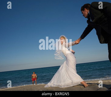 Bride and groom holding hands on beach, lifeguard in background Stock Photo