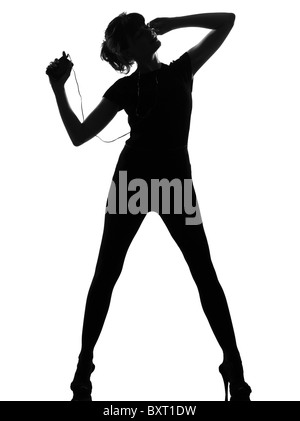 full length silhouette in shadow of a young woman ancing and listening music on mp3 audio player in studio on white background isolated Stock Photo