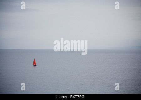 Sailing boat with red sail, sailing off the coast at Big Sand, Gairloch. Stock Photo