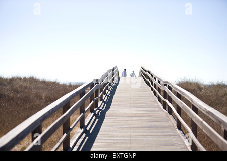 A wooden bridge over sand dunes, two people in the distance