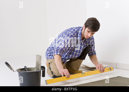 Home tile improvement - handyman with level laying down tile floor Stock Photo